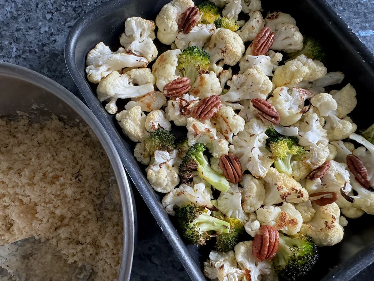 roasting tray of baked cauliflower florets with broccoli and toasted pecans