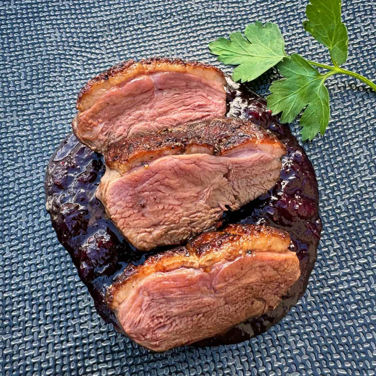 plate of 3 seared pink duck breast slices on top of a cherry sauce