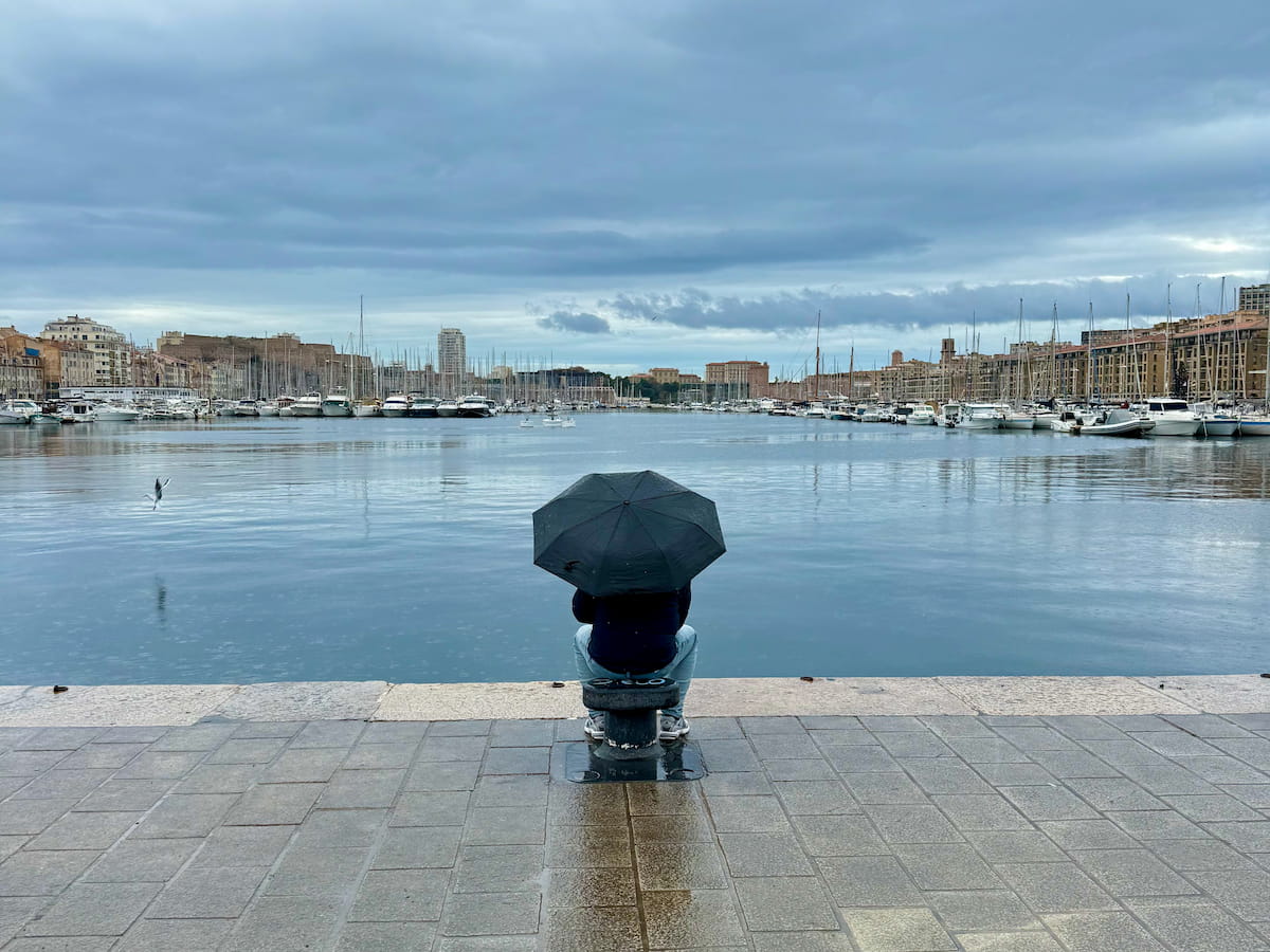 view of Marseille's vieux-port in the rain in winter, with someone sitting with an umbrella