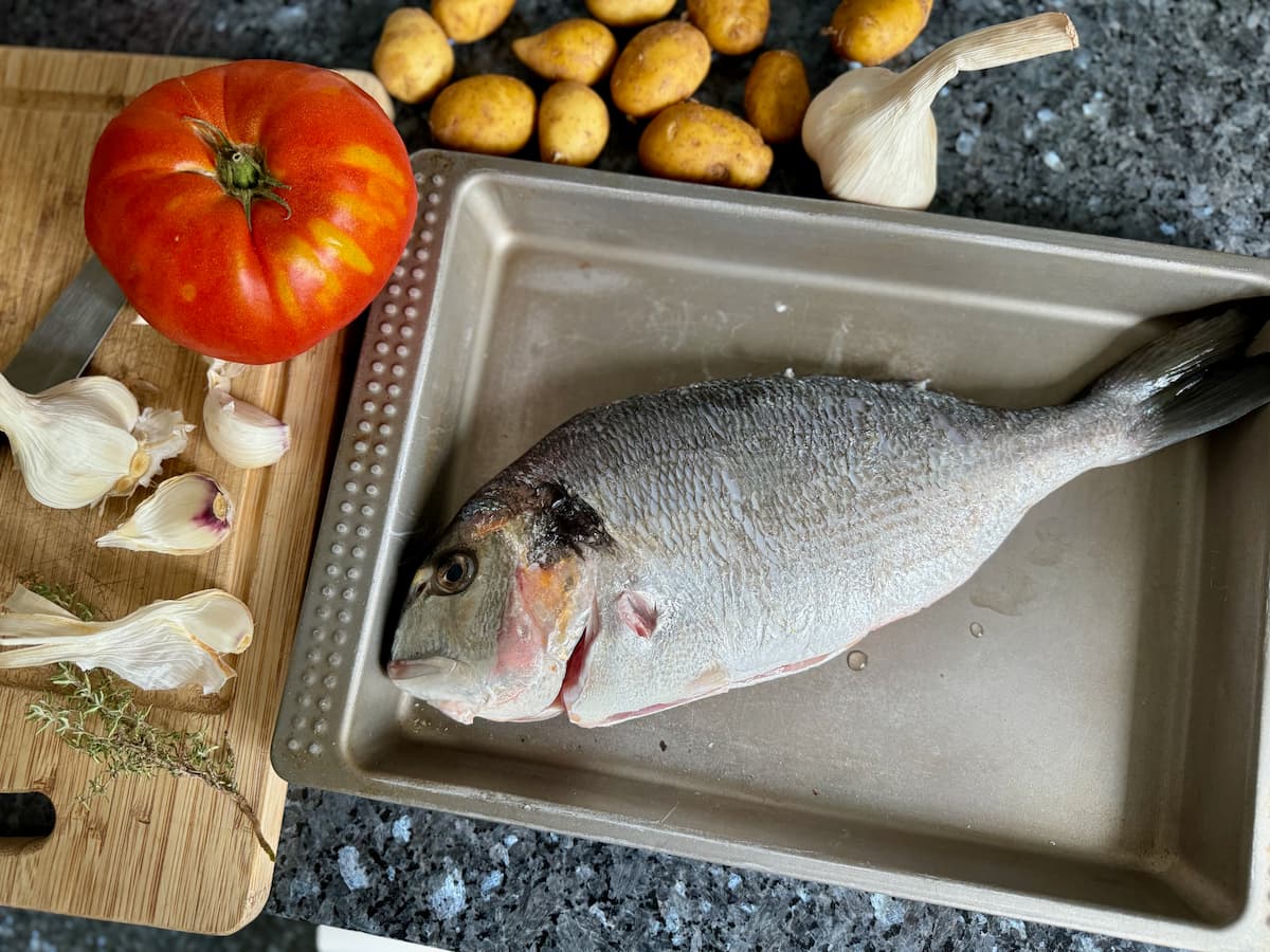sea bream in a sheet pan the size of the fish with tomato, garlic and potatoes