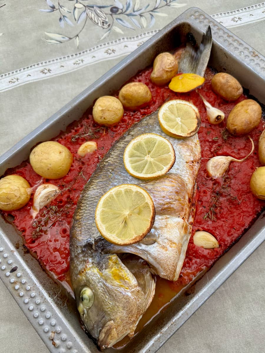 oven dish with baked sea bream fish in tomato sauce and topped with lemon