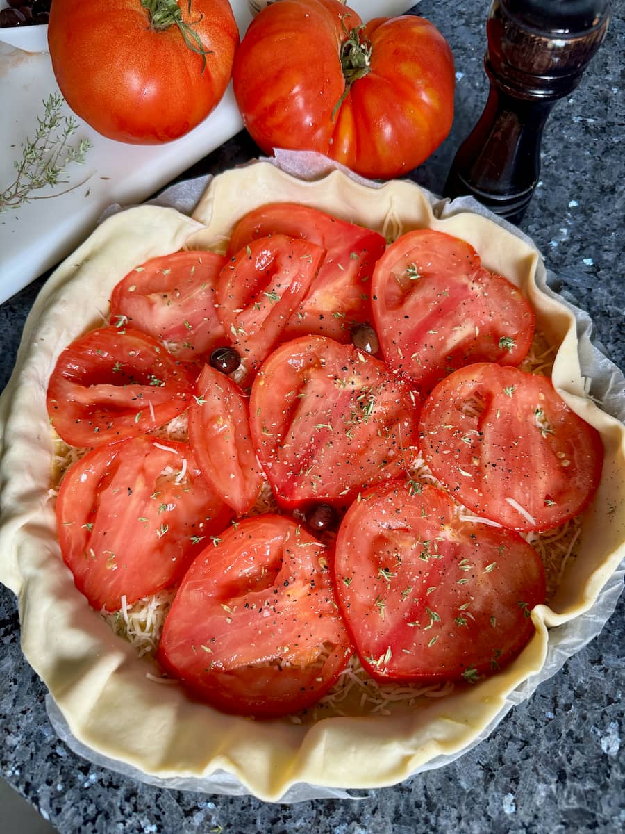 puff pastry in a pie dish topped with sliced tomatoes, mustard and fresh thyme herbs