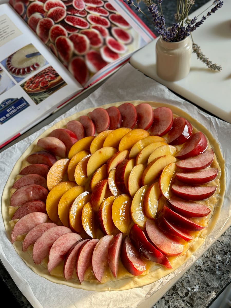 slices of white and yellow peach and nectarine arranged in a circle on puff pastry and almond cream