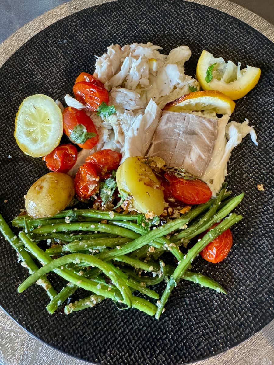 plate of prepared fluffy sea bass fish with roasted tomatoes, potatoes, lemon and sauteed green beans