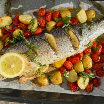 baked sea bass fish on one baking sheet with potatoes, cherry tomatoes, lemon and herbs