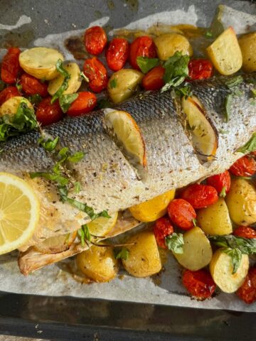 baked sea bass fish on one baking sheet with potatoes, cherry tomatoes, lemon and herbs