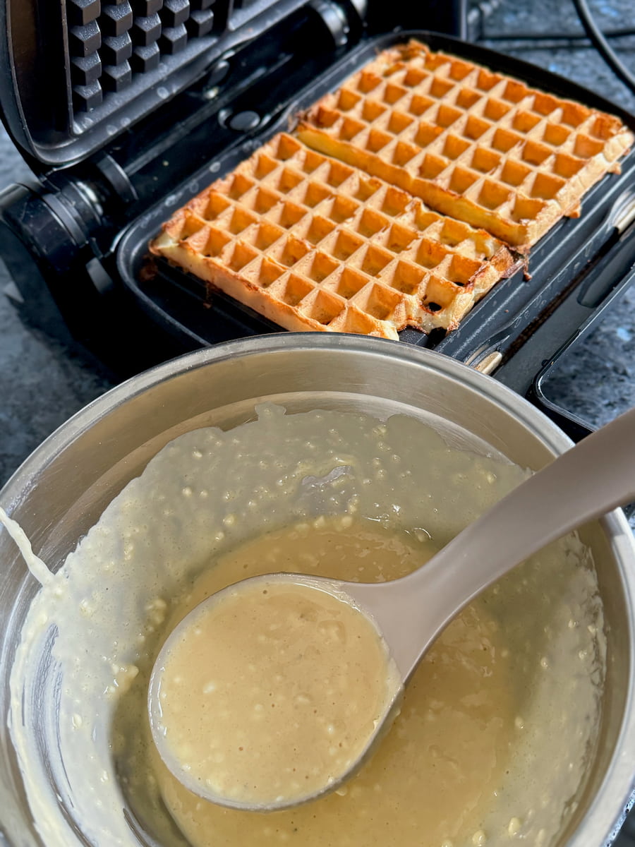 ladelling batter with cottage cheese curds showing onto a hot waffle iron