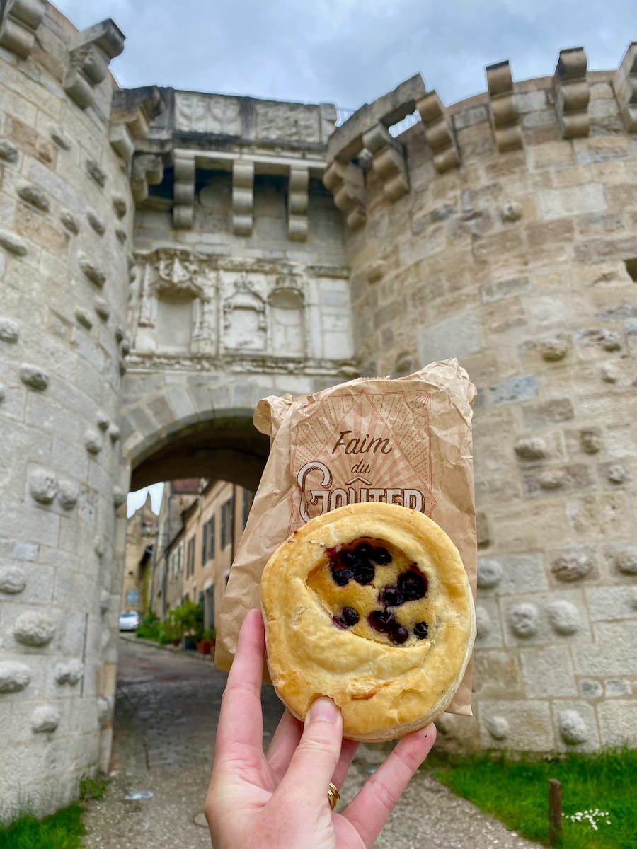 holding a French pastry in front of a medieval fortress in France