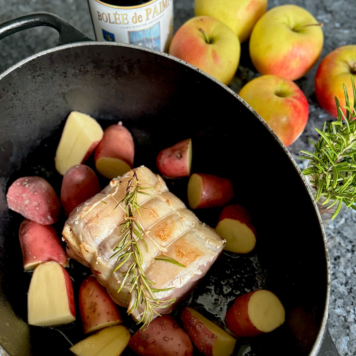 pork roast with rosemary and potatoes in a crock pot next to apples and cider