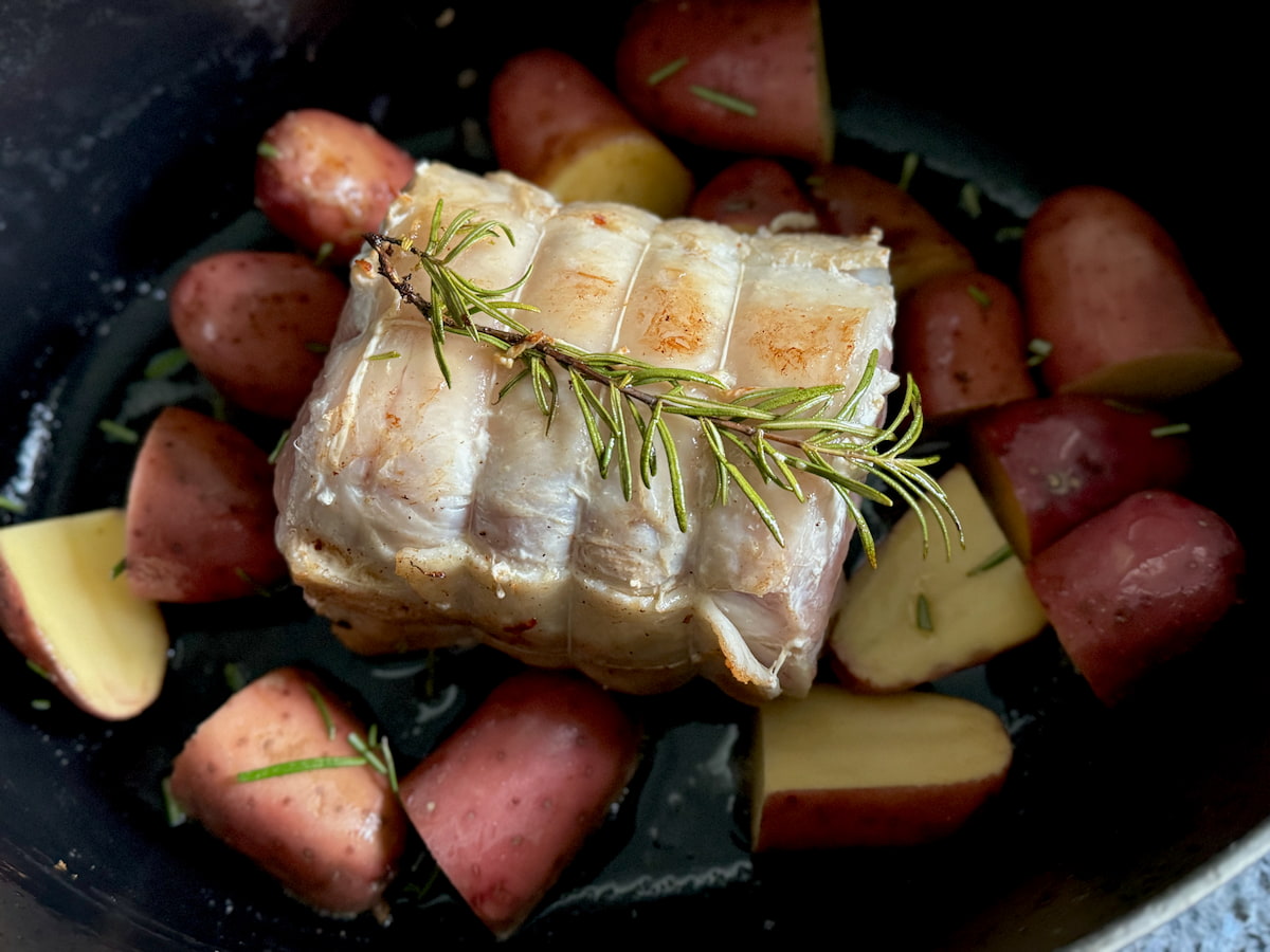 tied up pork roast shoulder in a crock pot with potatoes and rosemary