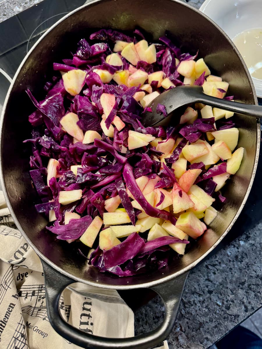 a crock pot mixed with cooking red cabbage, chopped apple and onions with spices, all mixed together rather than in layers