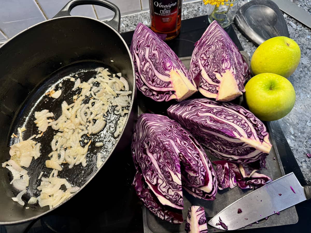 a chopped red cabbage next to apples and a crock pot with sliced onions cooking in oil