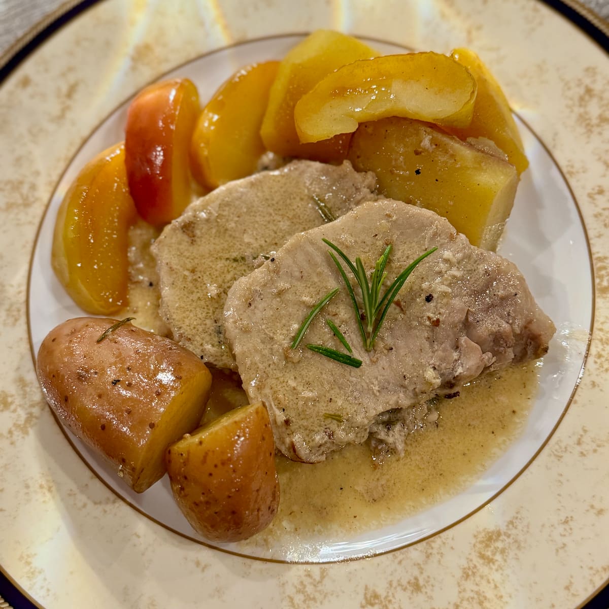 slices of cooked pork with rosemary, potatoes and apples in a cider sauce