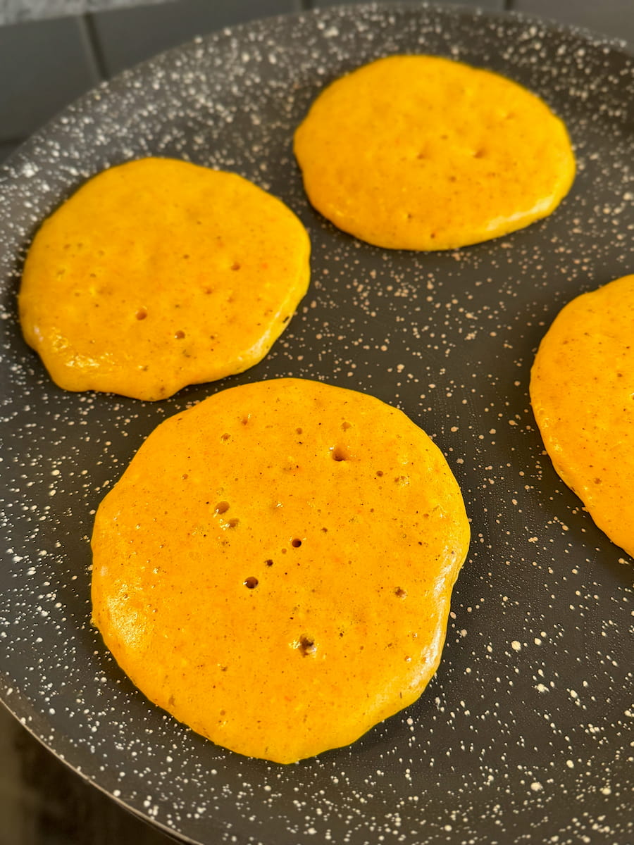 pumpkin pancakes in a non-stick pan with dough bubbling and making holes, a sign they're ready to turn
