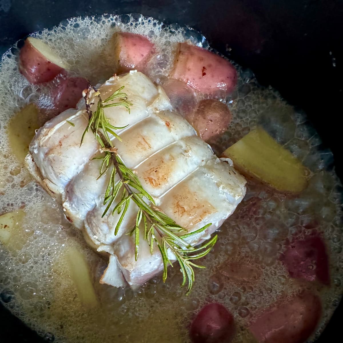 pork roast bubbling in a crock pot with apple cider, surrounded by potatoes and rosemary