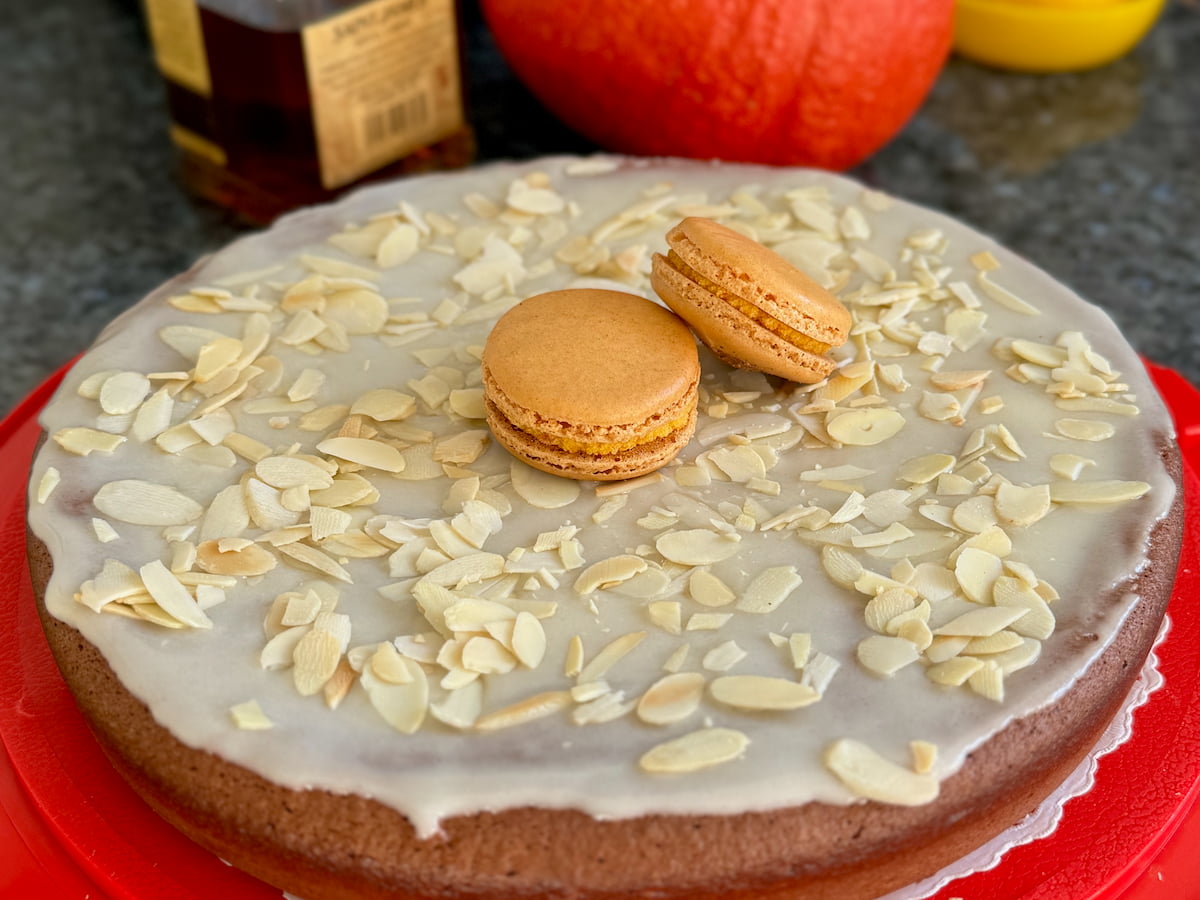 large round flourless chocolate cake with rum icing and flaked almonds topped with two pumpkin macarons