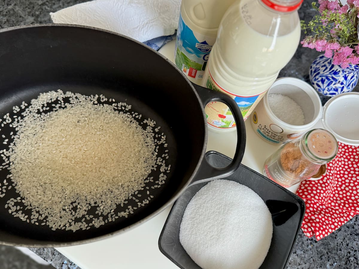 large cooking pot with short-grain rice, bowl of sugar, whole milk and cinnamon next to some salt.