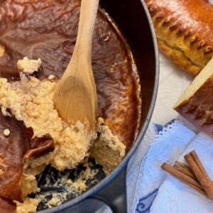 large pot with a baked rice pudding covered in a thick caramel skin, spooning out a creamy mixture underneath with cinnamon and a traditional French Fallue brioche