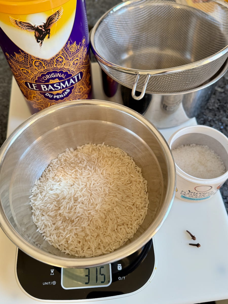measuring out exact quantity of Basmati rice for 4 portions on a kitchen scale next to salt, cloves and a pan with a sieve