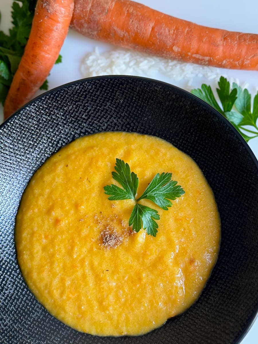 large black bowl of creamy carrot soup, thickened with rice and topped with fresh parsley