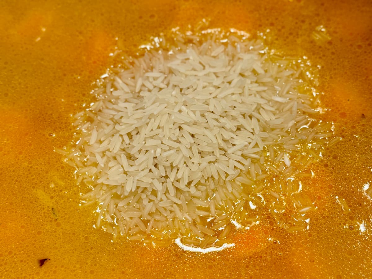 a close-up of a pot of carrots, onion and chicken stock topped with rice