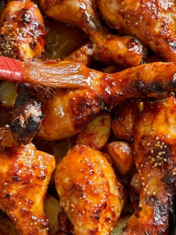 juicy chicken drumsticks being baked and brushed with a tomato BBQ sauce