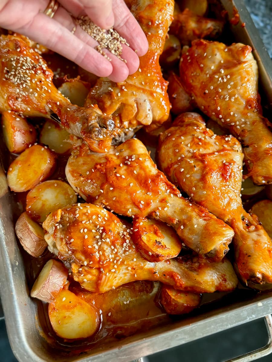 sprinkling sesame seeds over roasting chicken drumsticks marinated in a BBQ sauce