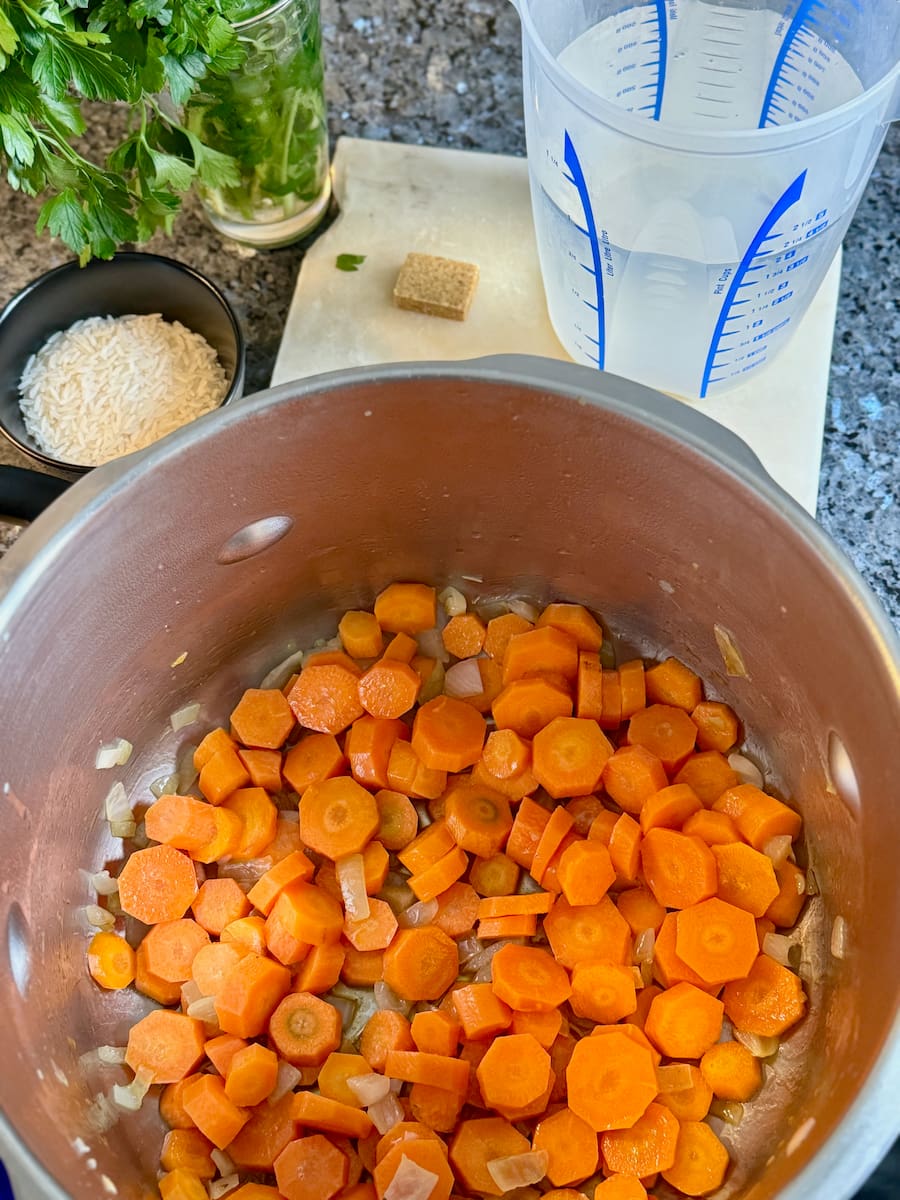 chopped carrots in a large soup pan, tossed in melted butter and cooked onion next to chicken stock and rice