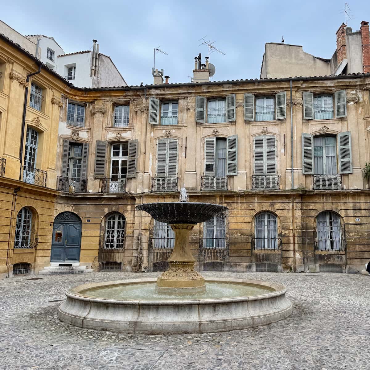cobbled square with a fountain and old buildings with blue shutters in Aix-en-Provence