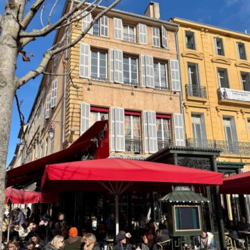 bustling café in Aix-en-Provence in the sunshine with people drinking coffee outside next to a plane tree