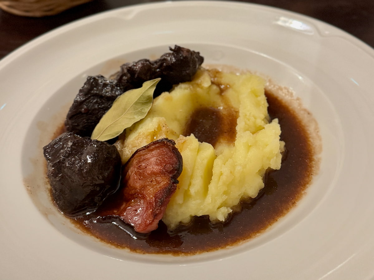 bowl dish with a dark coloured beef stew, bacon and mashed potato, a Provencal daube