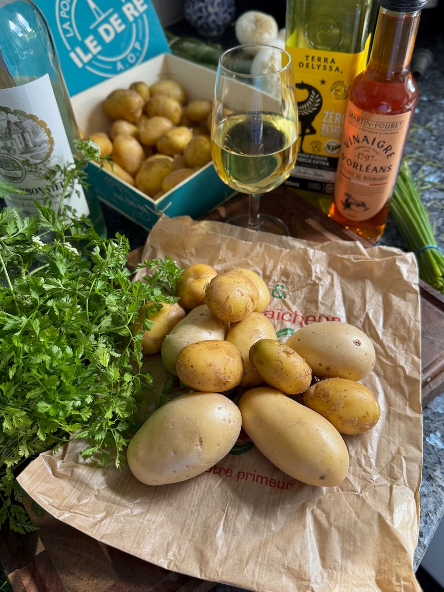 ingredients laid out to make a classic French potato salad: small new potatoes, white wine, vinegar, olive oil, fresh parsley, chervil and chives
